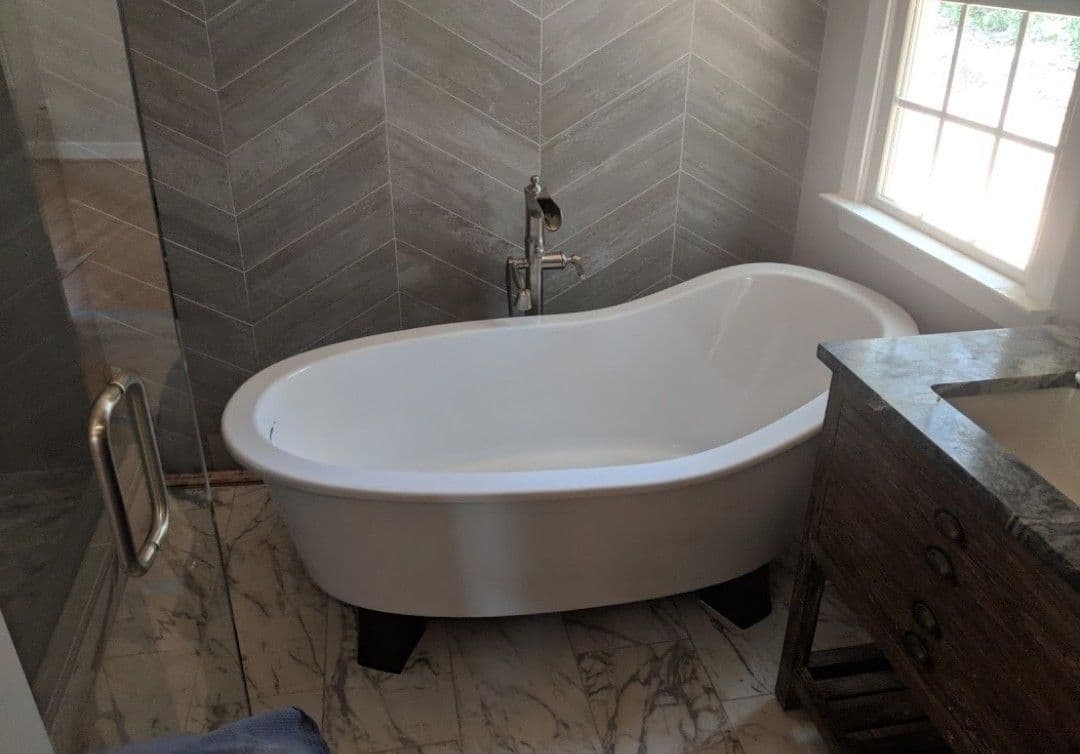 Modern freestanding bathtub in a chic bathroom with marble flooring and herringbone tile walls.
