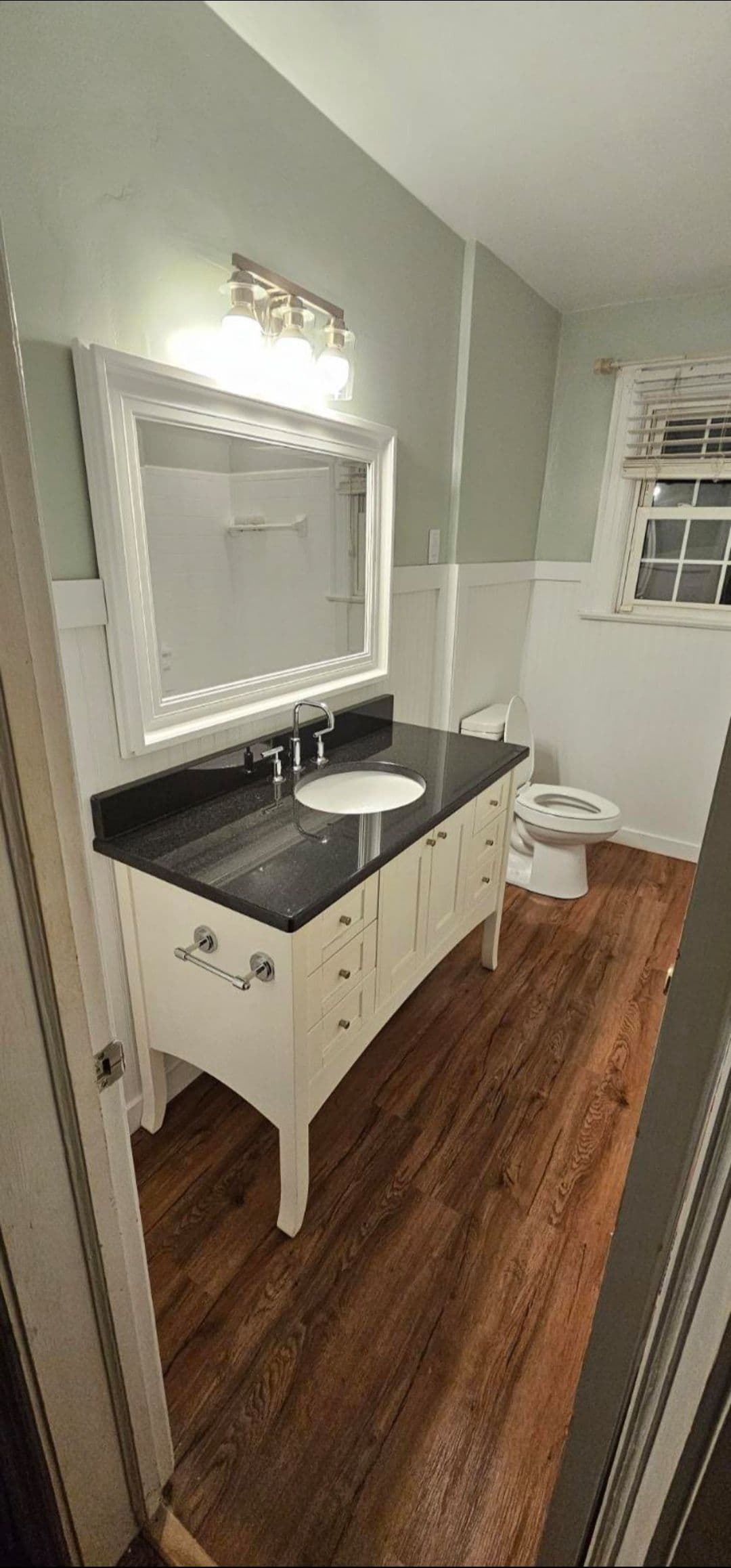 Modern bathroom featuring white vanity with black countertop and wood flooring.
