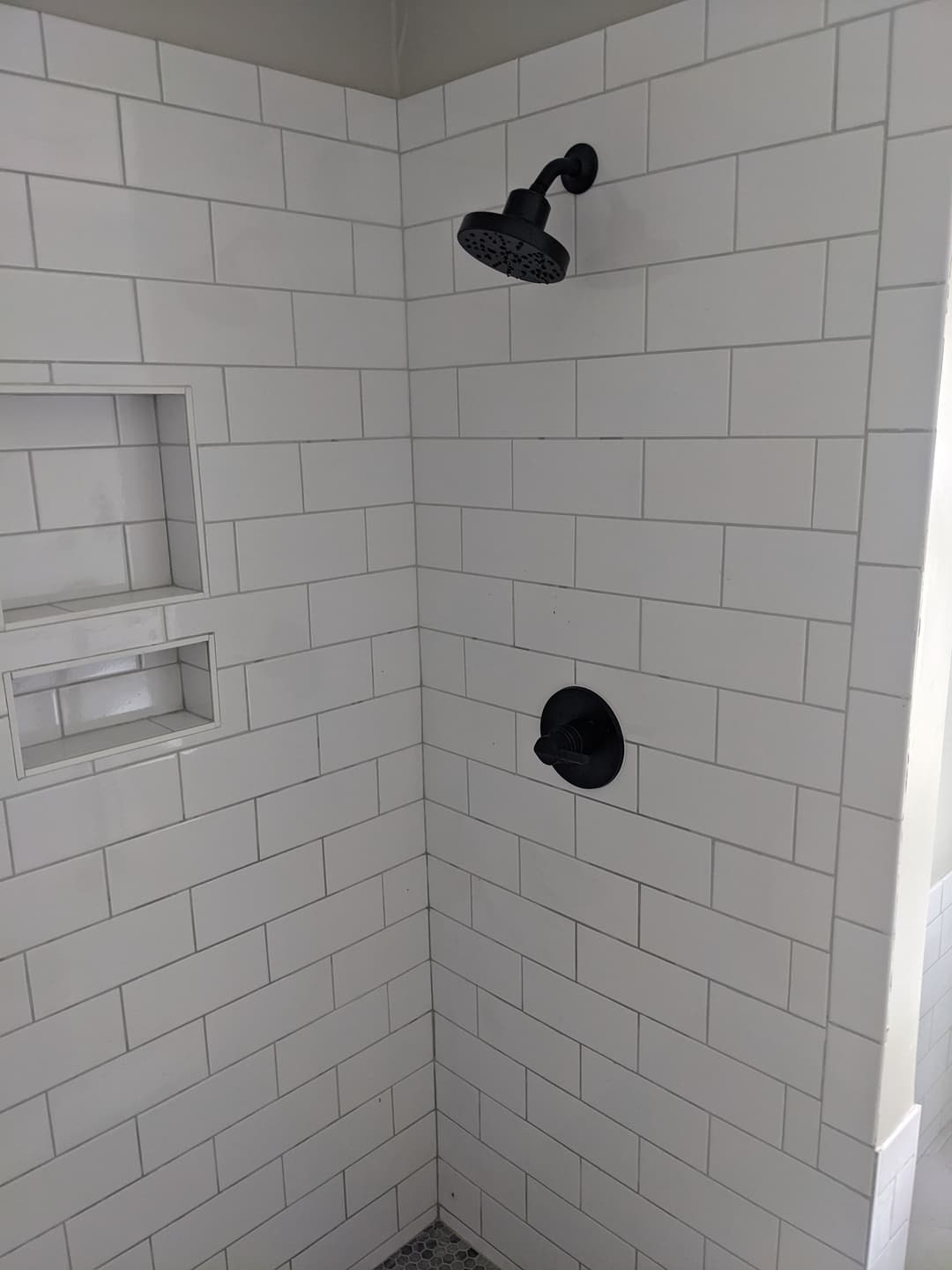 Modern shower corner featuring black fixtures and white subway tile walls.