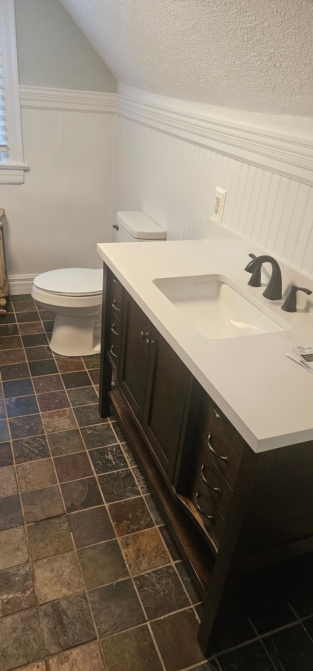 Modern bathroom featuring a dark wood vanity, sleek sink, and slate tile flooring.