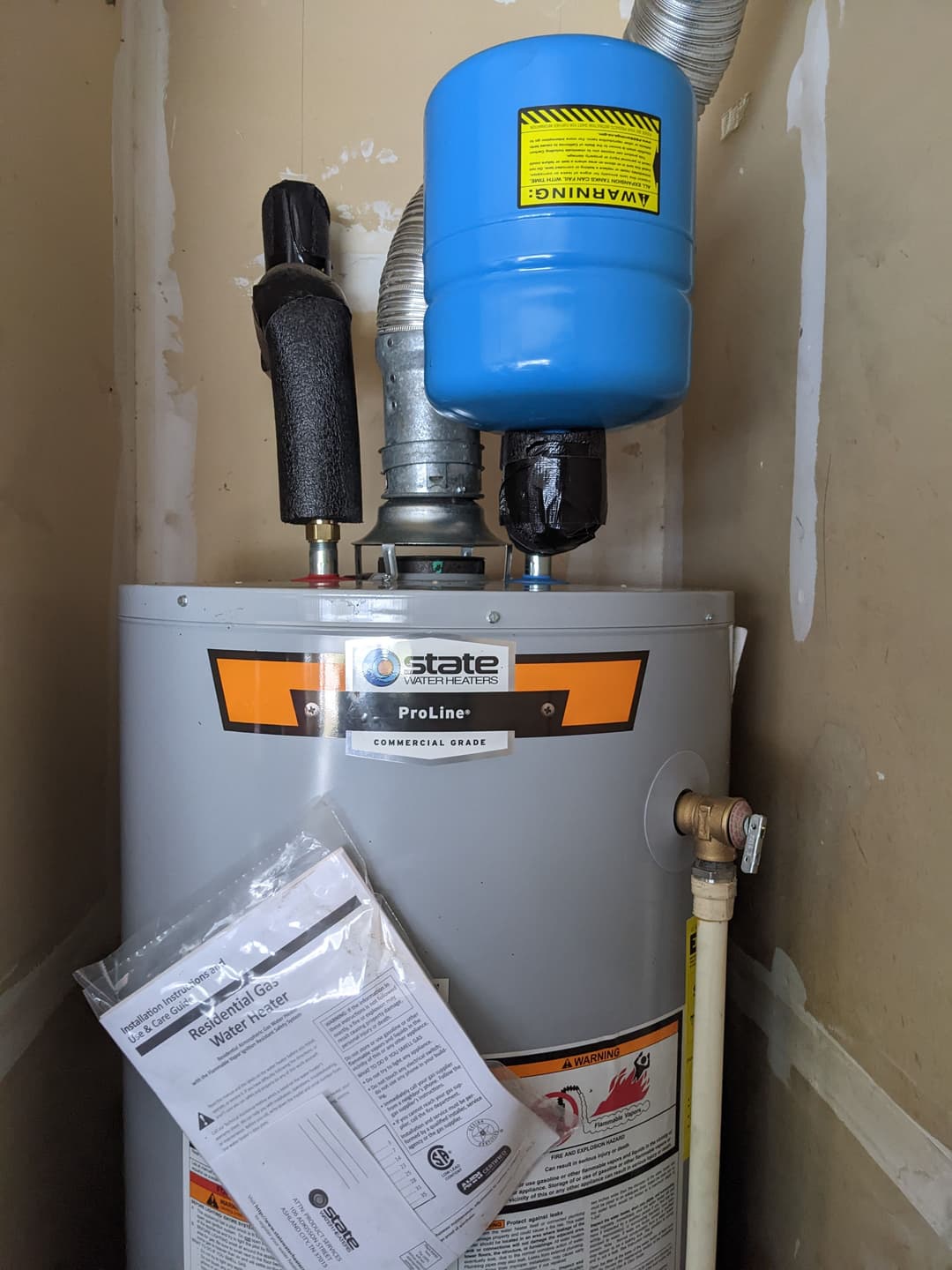Proline commercial gas water heater installed with instruction manual nearby.