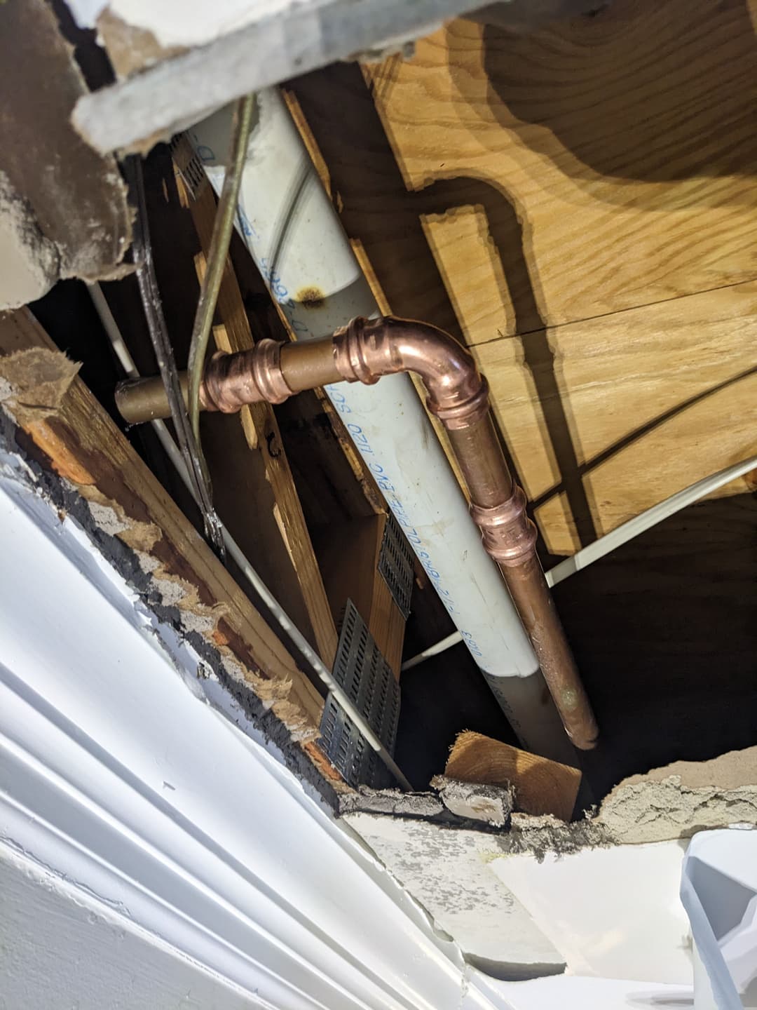 Exposed plumbing with copper pipes and wooden structure in a damaged wall.
