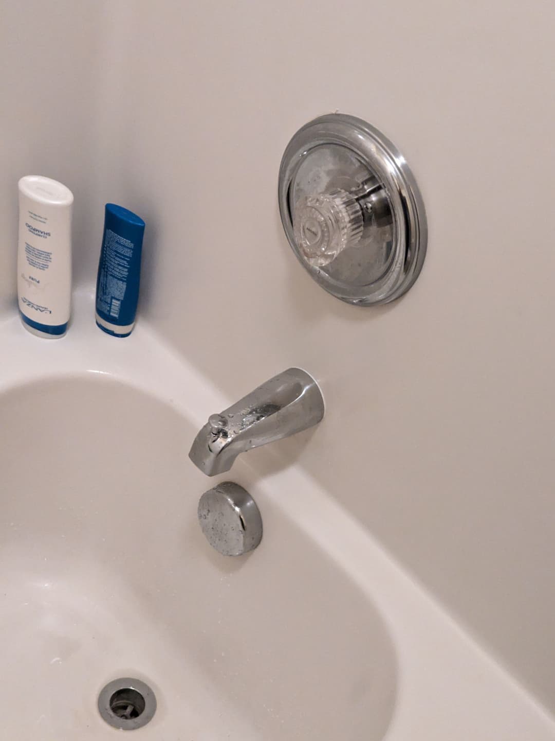 Shower faucet and controls in a modern bathroom with shampoo containers nearby.