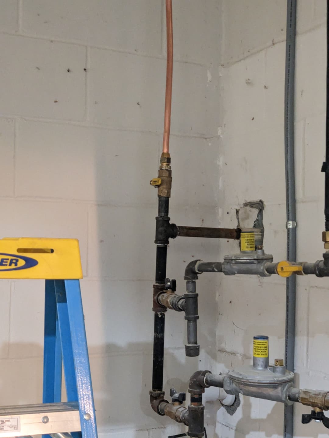 Pipes and valves in a home plumbing system, with a ladder in the background.
