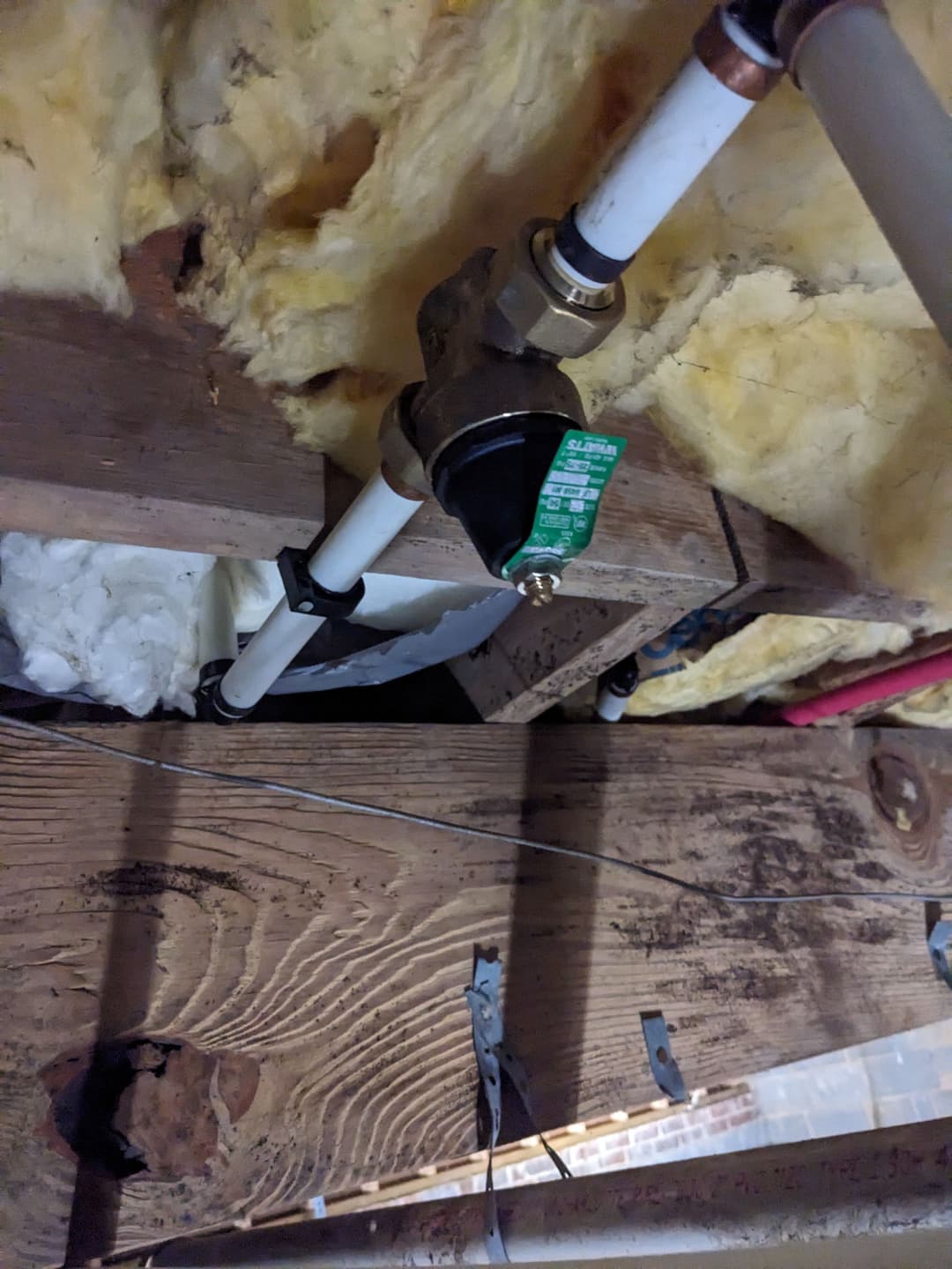 Water valve installation with PVC pipes in attic insulation and wooden beams.