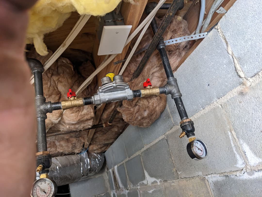 Gas line setup with pressure gauges and valves in a basement, showing insulation and plumbing details.
