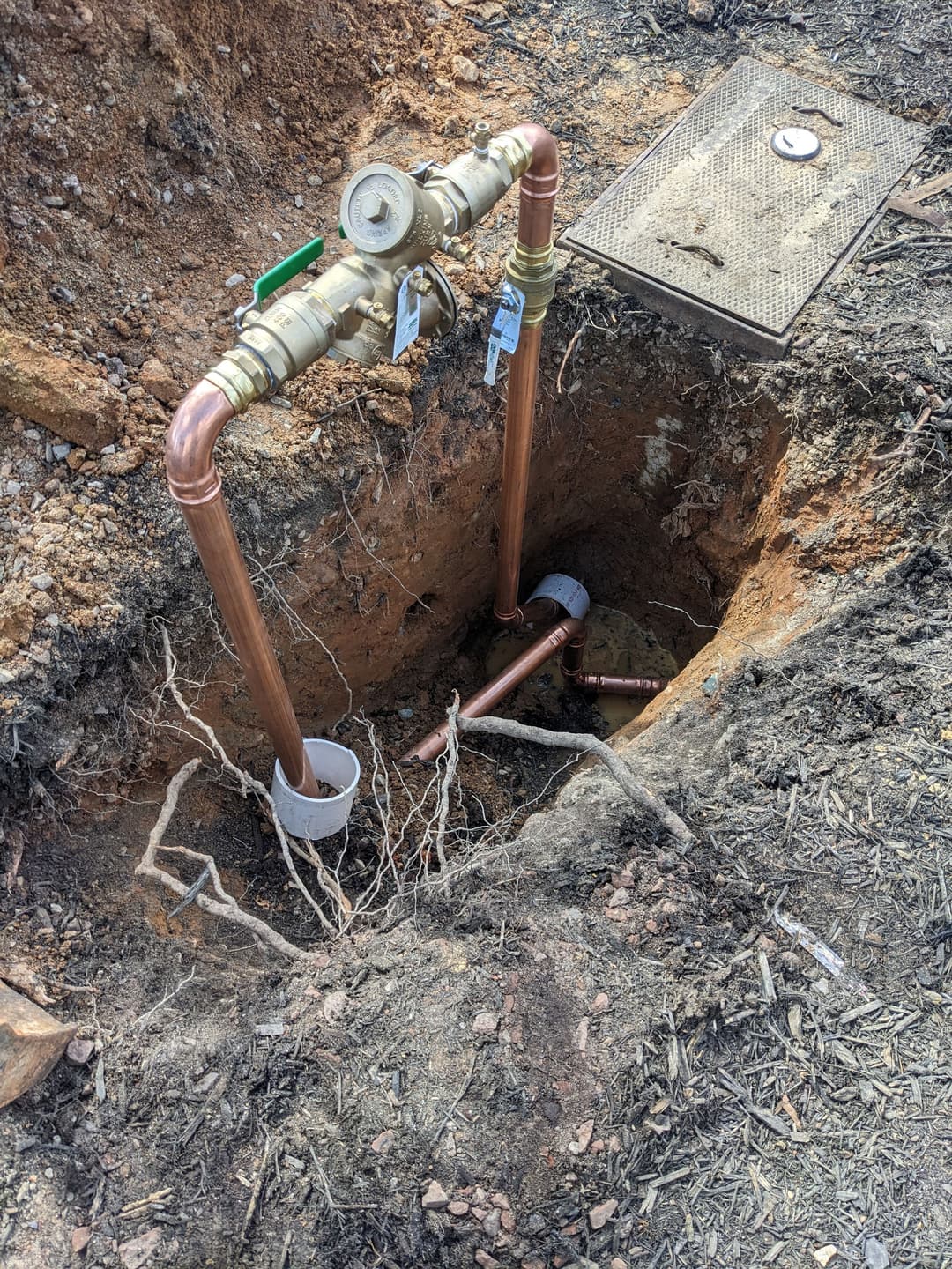 Copper plumbing installation in a trench with a valve and roots nearby.