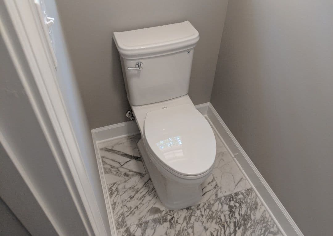 Modern white toilet with sleek design in a gray interior and marble floor.