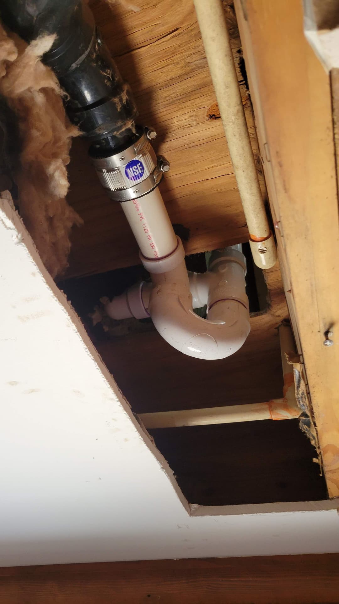 Pipe plumbing installation in ceiling with visible PVC and metal fittings.