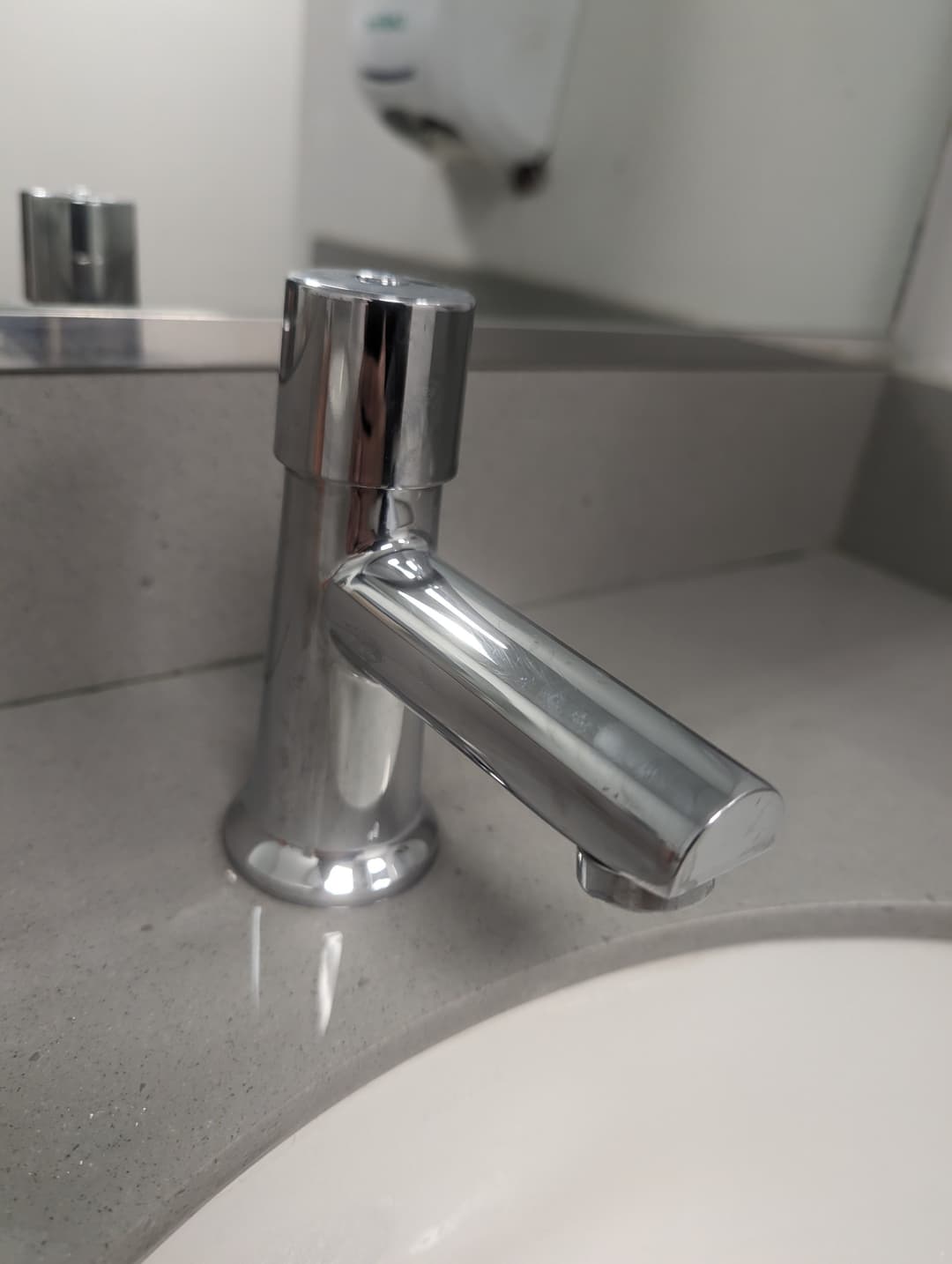 Chrome bathroom faucet on a gray countertop with a mirror in the background.