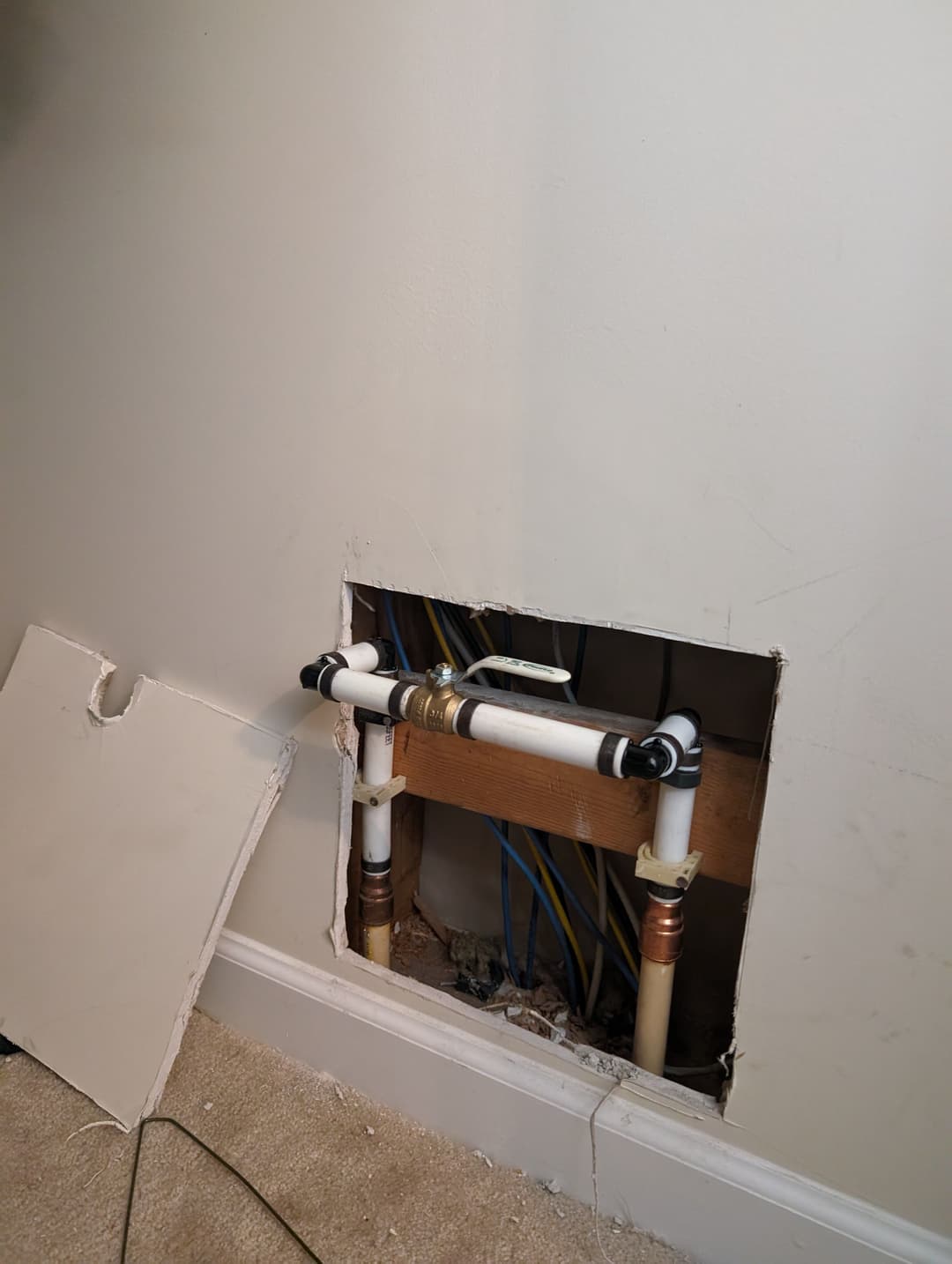 Exposed plumbing pipes inside wall with a cutout section and surrounding drywall.