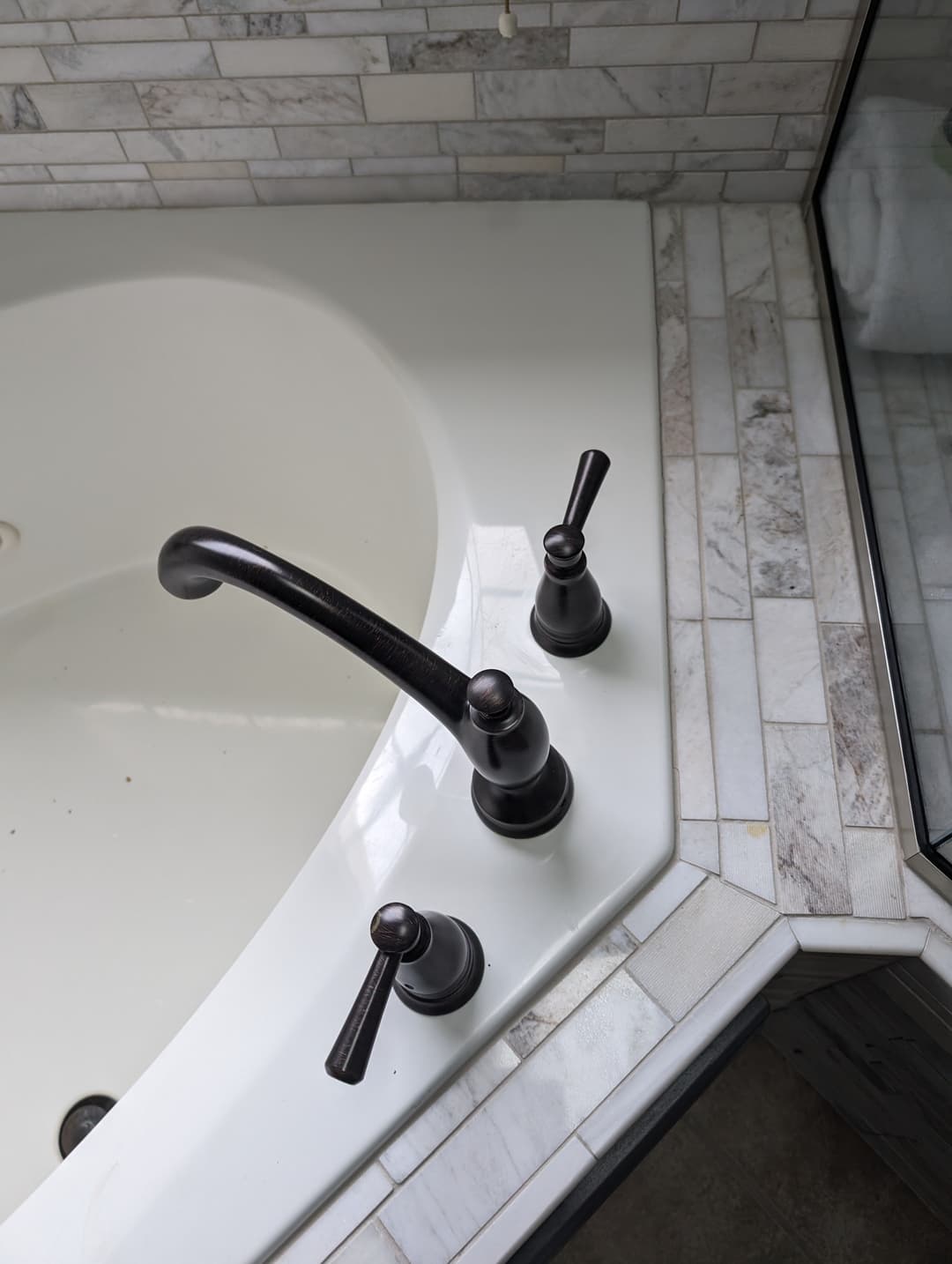 Modern bathtub faucet with bronze fixtures, white tub, and tiled surroundings.