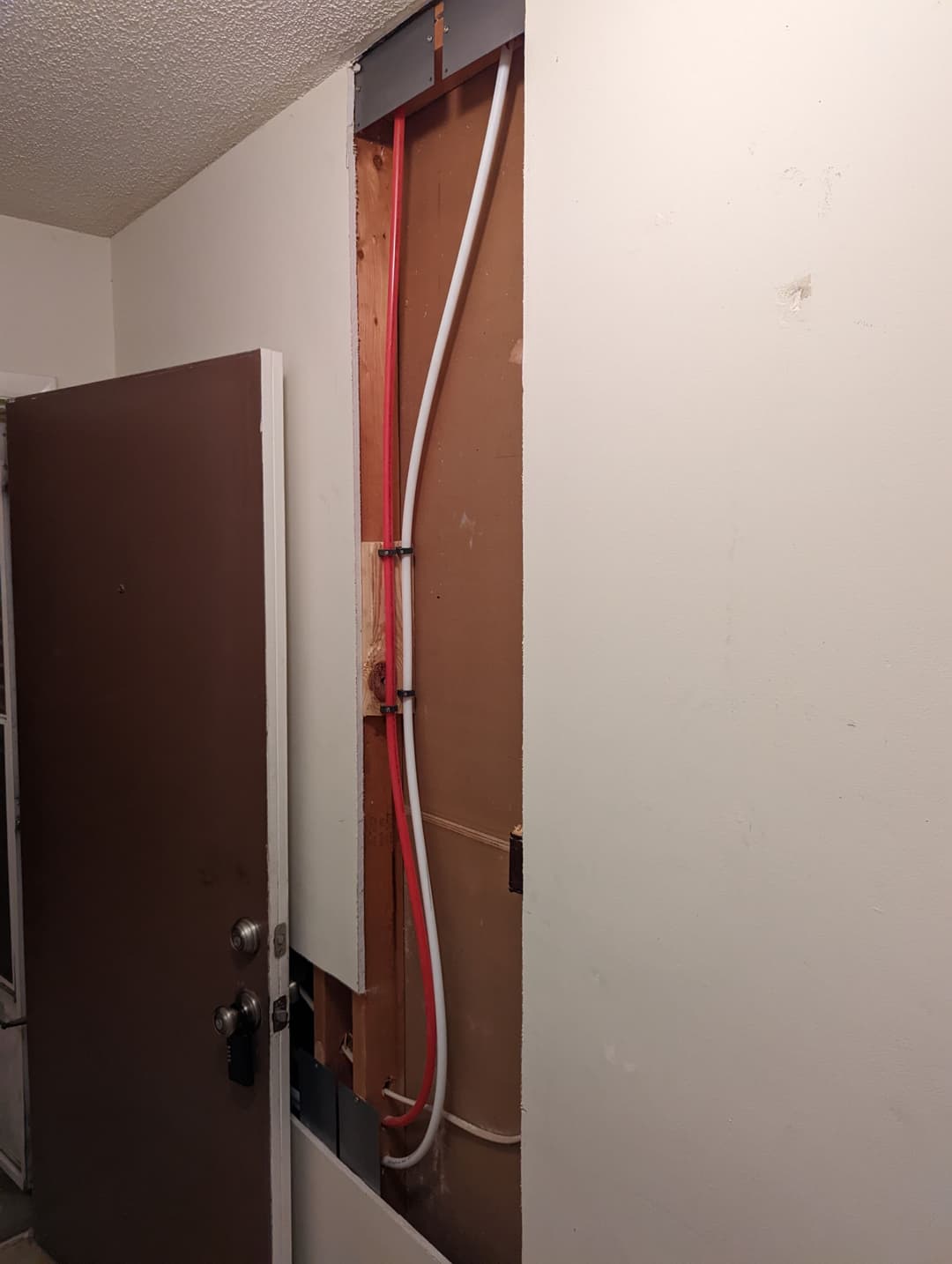 Exposed wall section showing plumbing pipes and electrical lines in a residential entryway.