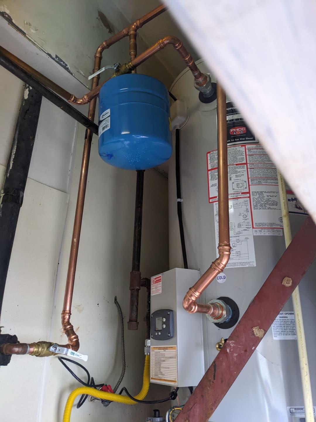 Installation of a copper plumbing system and blue expansion tank in a residential utility room.