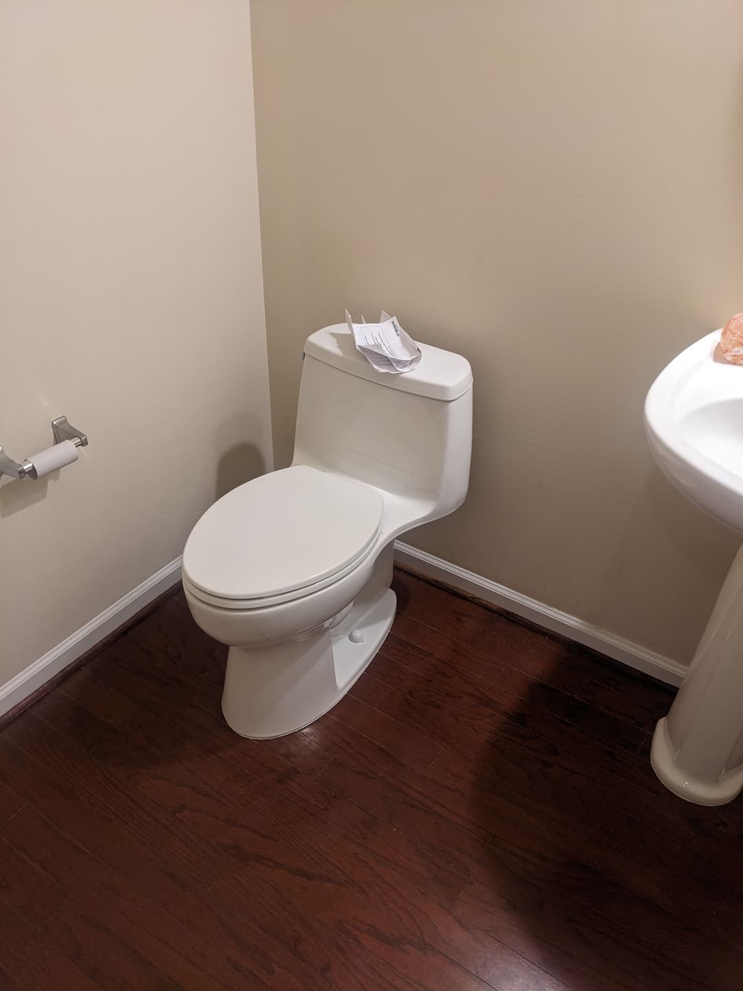 Modern white toilet in a minimalistic bathroom with hardwood flooring and a sink.