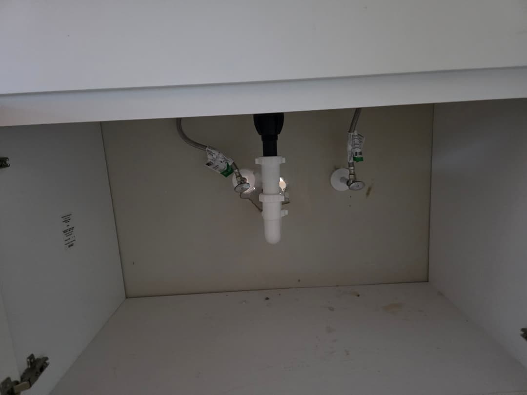 Plumbing setup under a sink with shutoff valves and a central connector pipe.