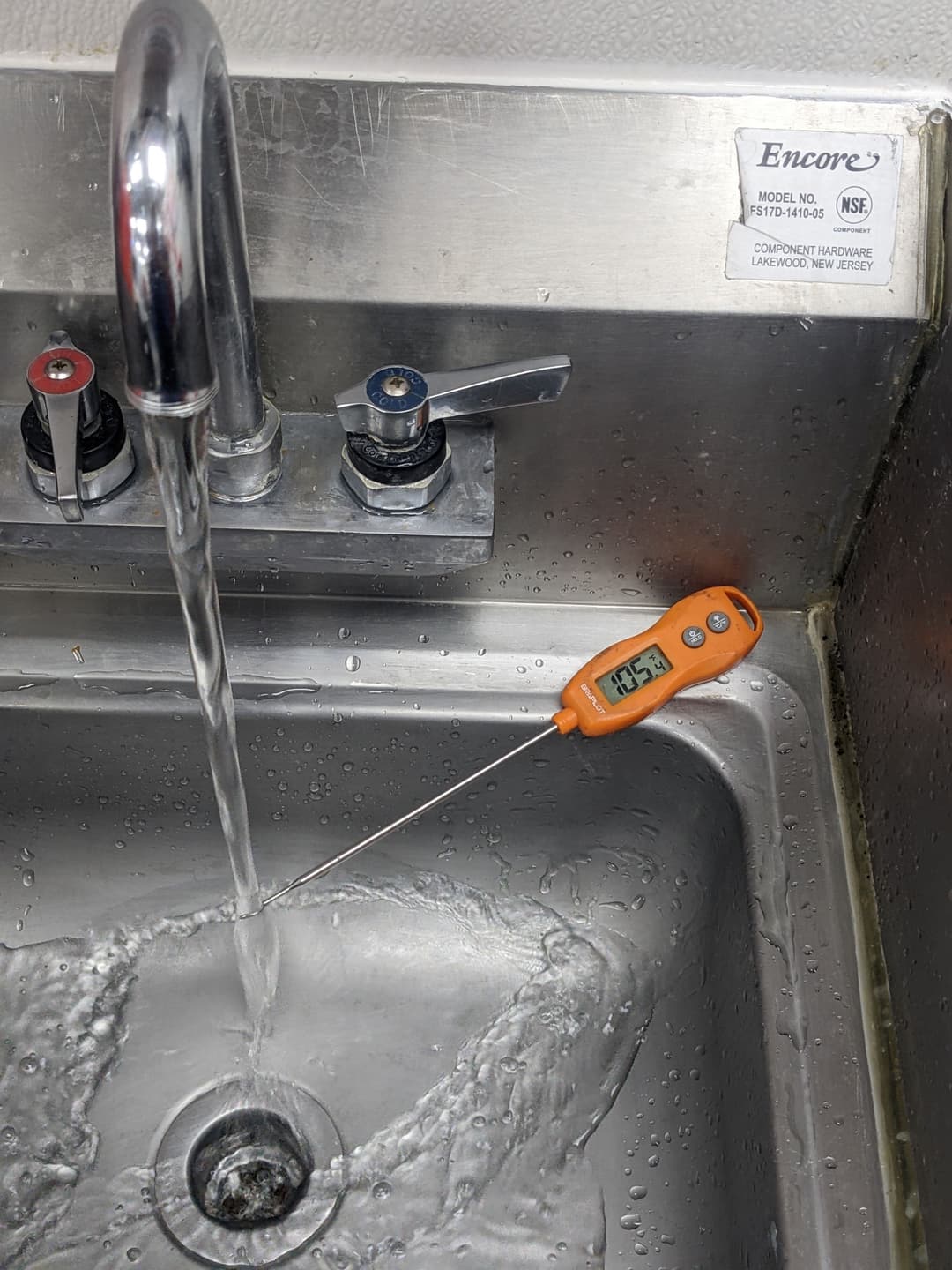 Water flow from a faucet with a digital thermometer measuring temperature in a stainless steel sink.