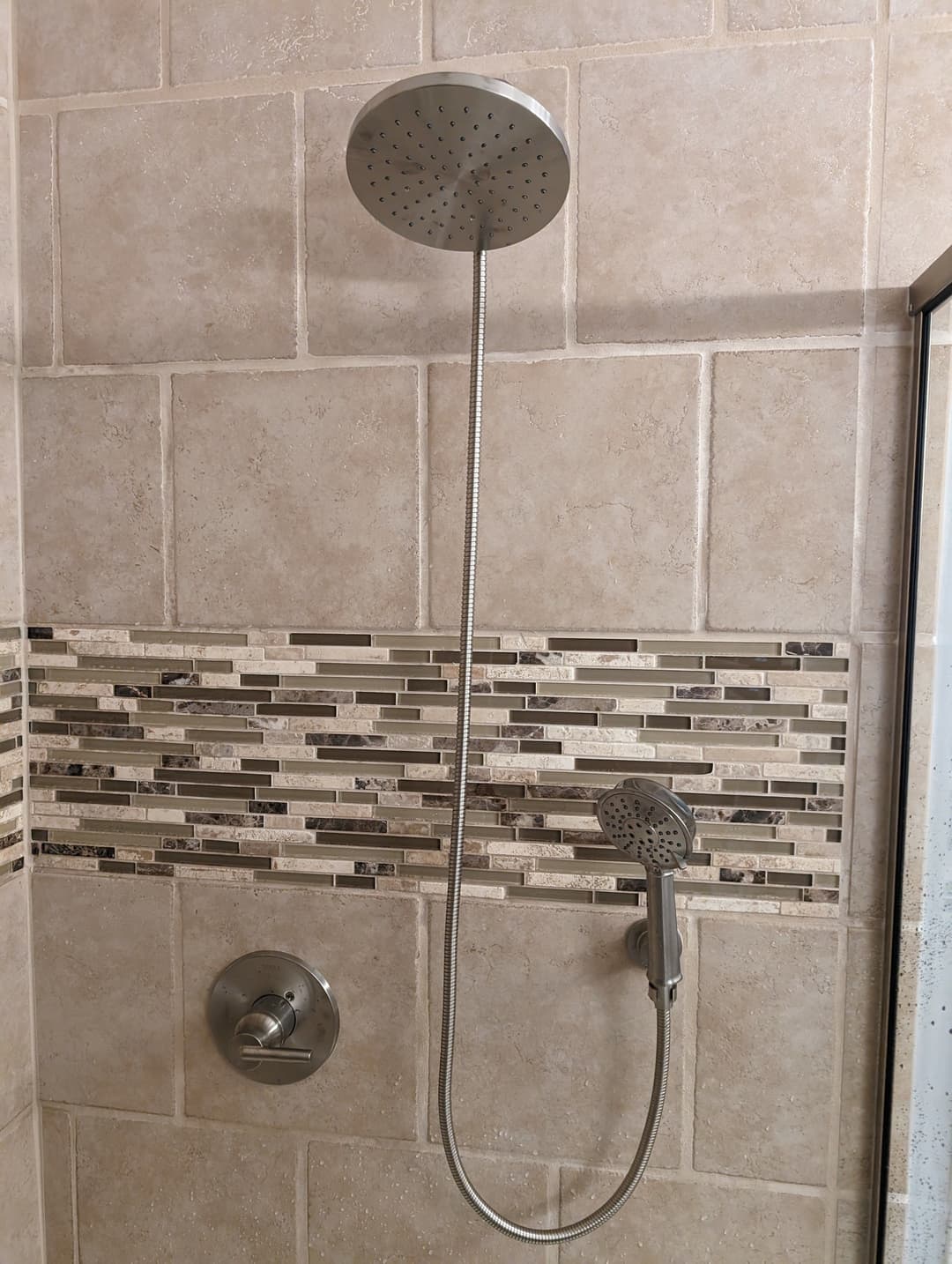 Modern shower fixture with a rain showerhead and handheld sprayer on tiled wall.