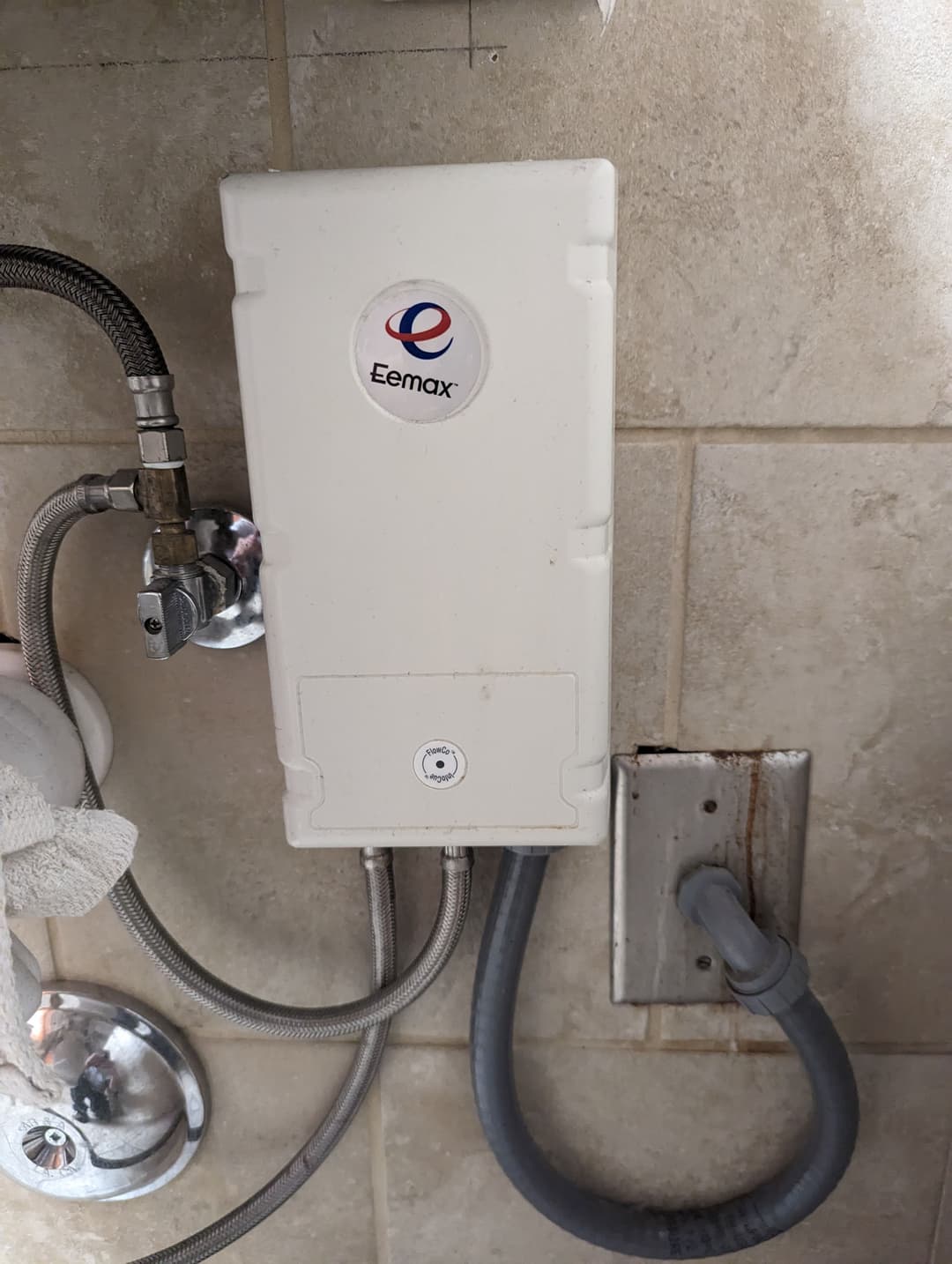 Eemax tankless water heater mounted on bathroom wall with plumbing connections.
