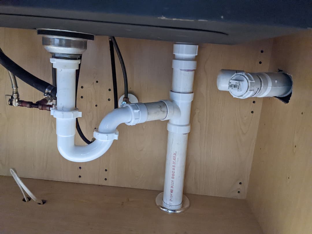 Under-sink plumbing with PVC pipes and fittings, featuring a sink drain and connection to disposal.