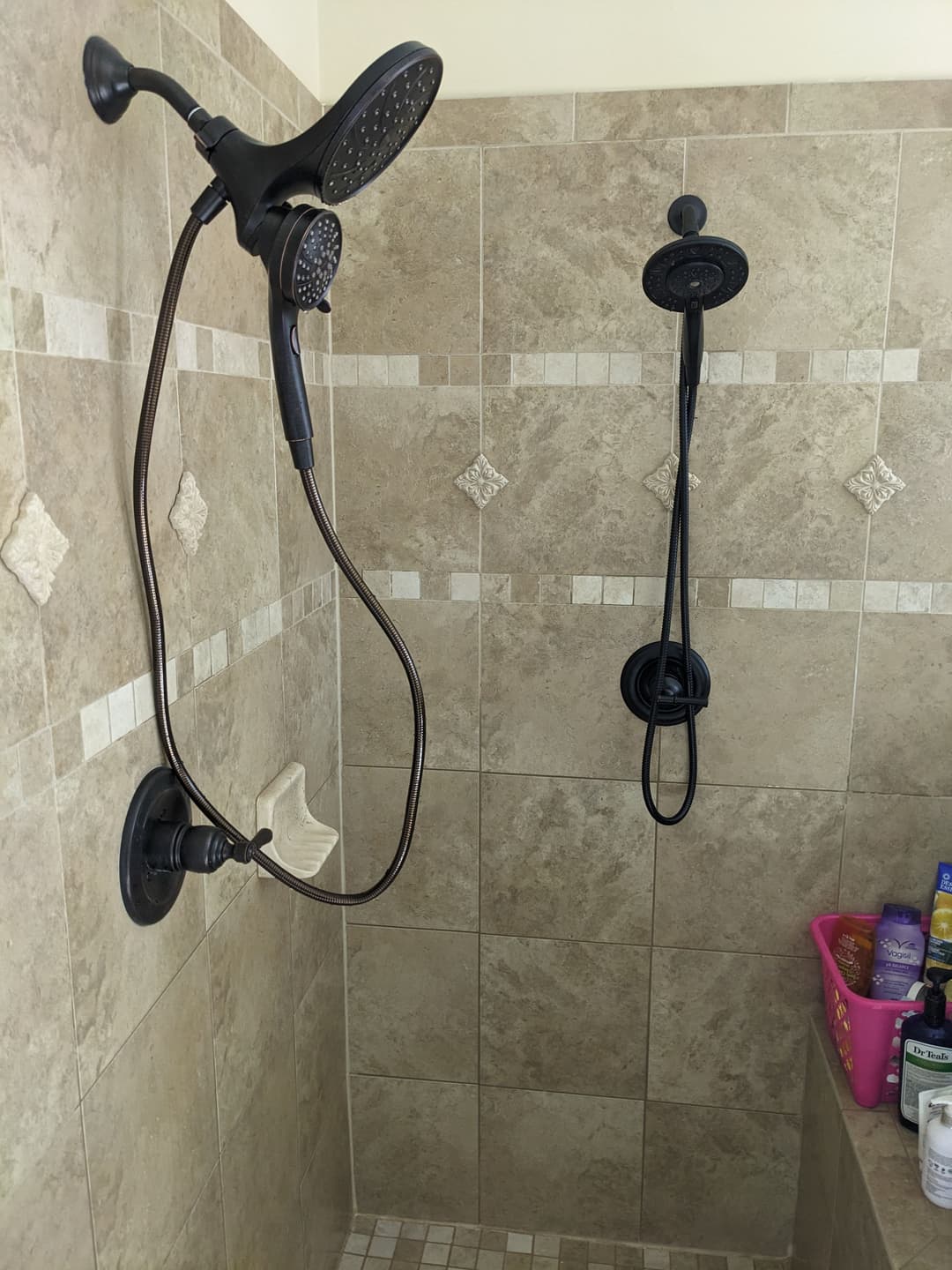 Modern shower with dual showerheads and stone tile walls, featuring a corner shelf and toiletries.