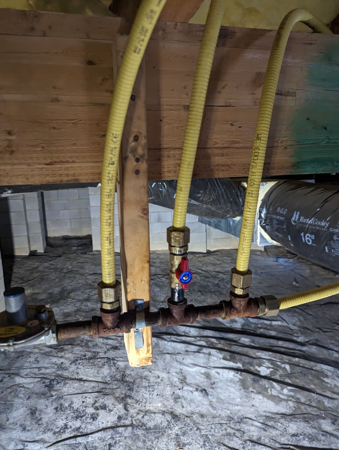 Gas line connections with yellow tubes and valves under a house basement.